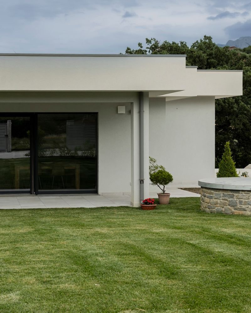Esterno di una casa moderna in muratura con ampie vetrate e giardino curato