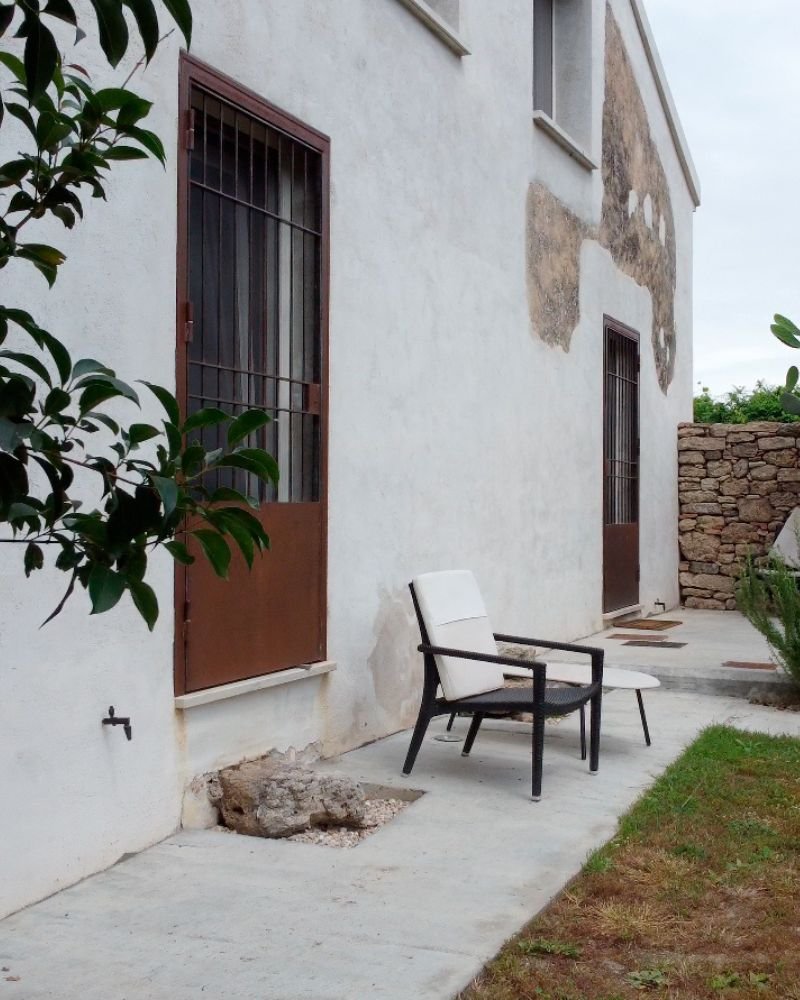 Patio esterno di casa ristrutturata con sedie e tavolino, porte in ferro e giardino circostante