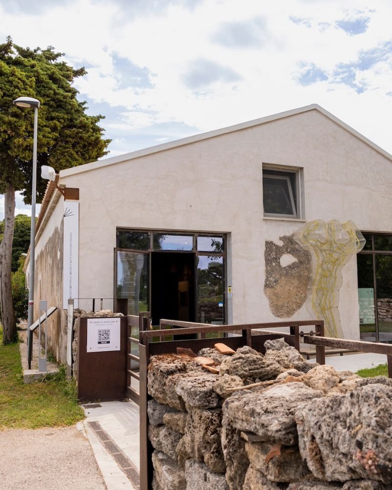 Vista esterna dell'ingresso di un casale restaurato con mura in pietra, intonaco bianco e decorazioni artistiche