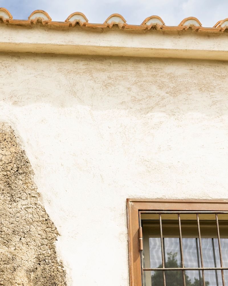 Primo piano di finestra con grata in ferro e dettaglio delle mura restaurate in pietra e intonaco chiaro







