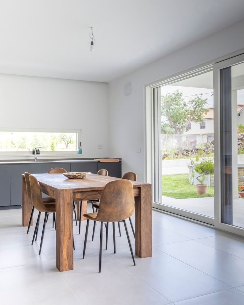 Sala da pranzo con arredi in legno e grandi vetrate che si affacciano sul giardino, in una casa in muratura moderna