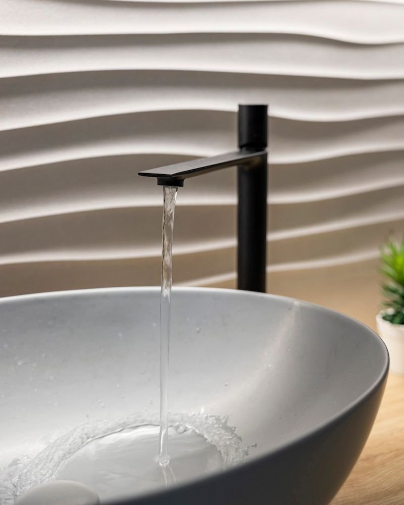 Primo piano di un lavabo dal design moderno con parete decorata a onde e rubinetto nero, in casa in muratura